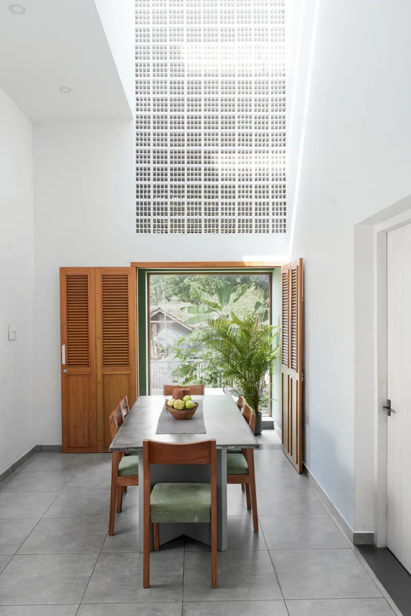 Dining room with wooden table and shuttered window beneath a perforated white ceiling panel
