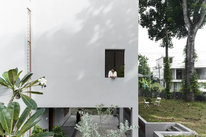 White facade with single window and person looking out above a recessed ground floor garden