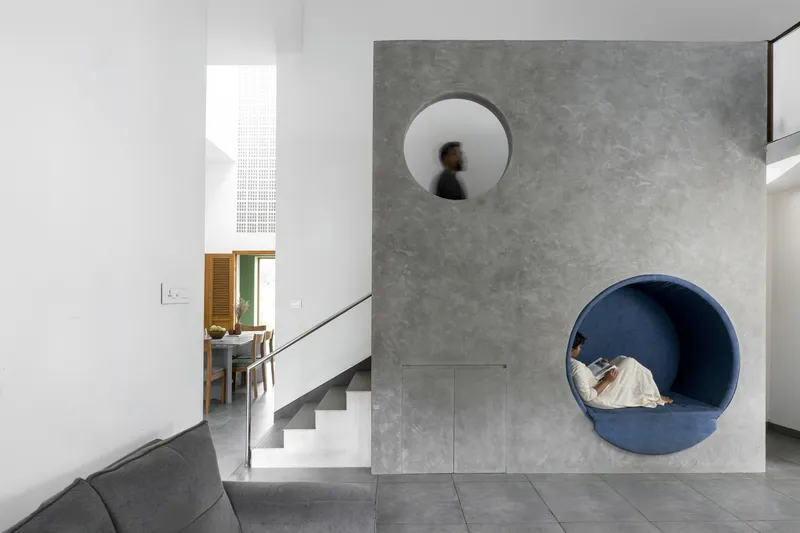 Grey concrete panel with circular openings framing a stair and adjacent dining space