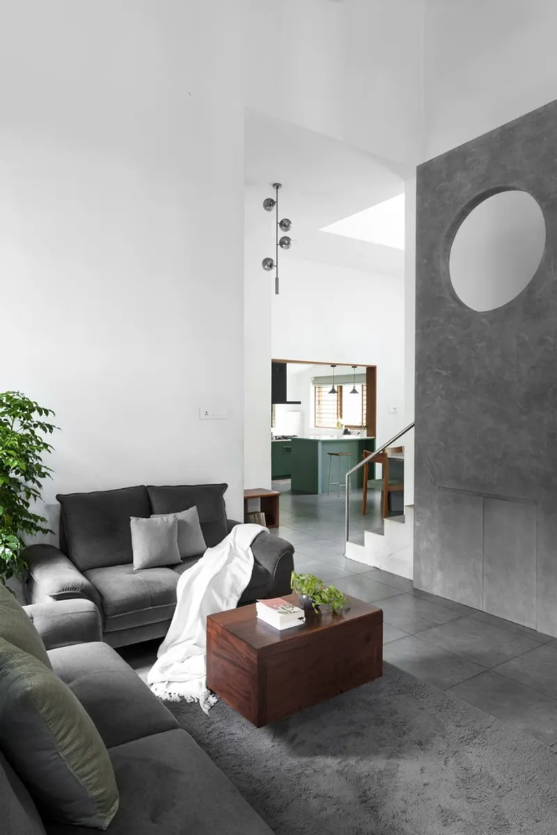 Double-height living room with circular opening in the concrete wall and view to kitchen beyond