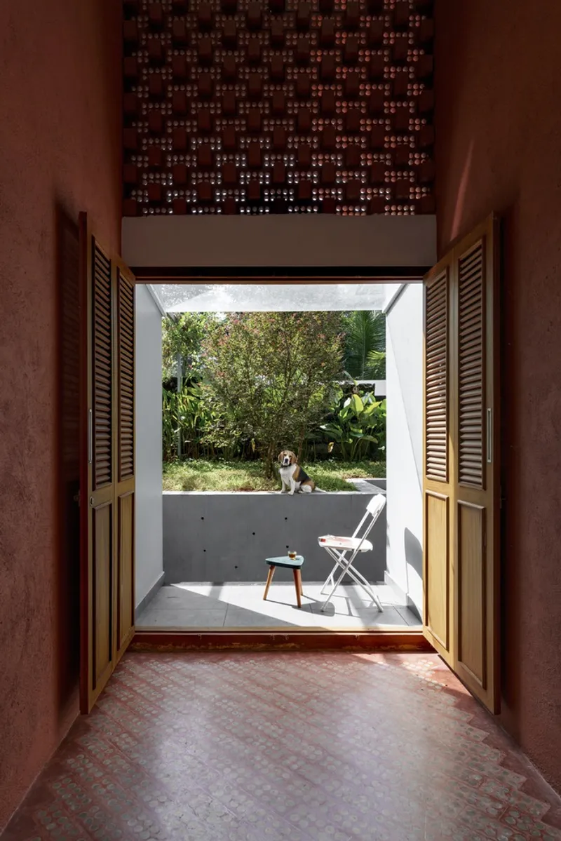 View through open timber shutters to a concrete balcony with dog and garden beyond