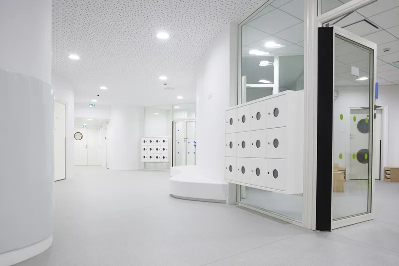 White reception area with perforated acoustic ceiling panels and circular port-hole details on partition wall