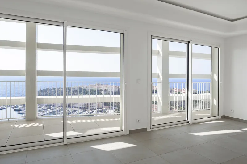 Empty interior room with floor-to-ceiling sliding glass doors opening to terrace overlooking marina and sea