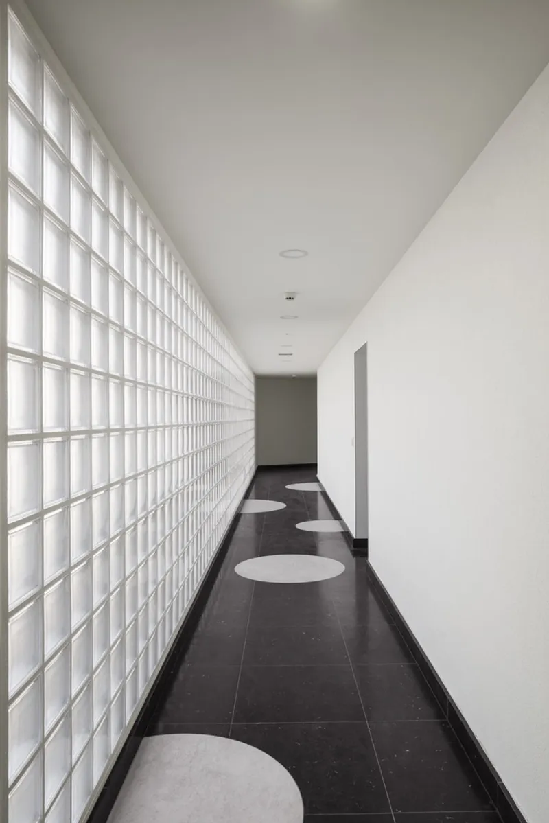 Corridor with translucent glass block wall on one side and circular floor inlays in dark tile