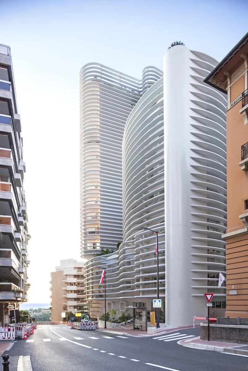 Street view of the curved tower with horizontal white louvers wrapping the facade at a pedestrian crossing