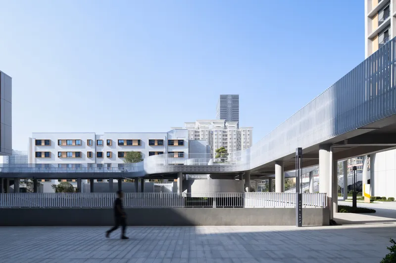 Elevated pedestrian bridge connecting white volumes with punched window openings against a backdrop of high-rise towers