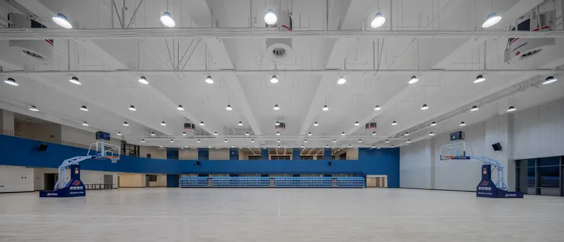 Basketball gymnasium with retractable bleachers, exposed truss ceiling and blue painted accent walls flanking the court