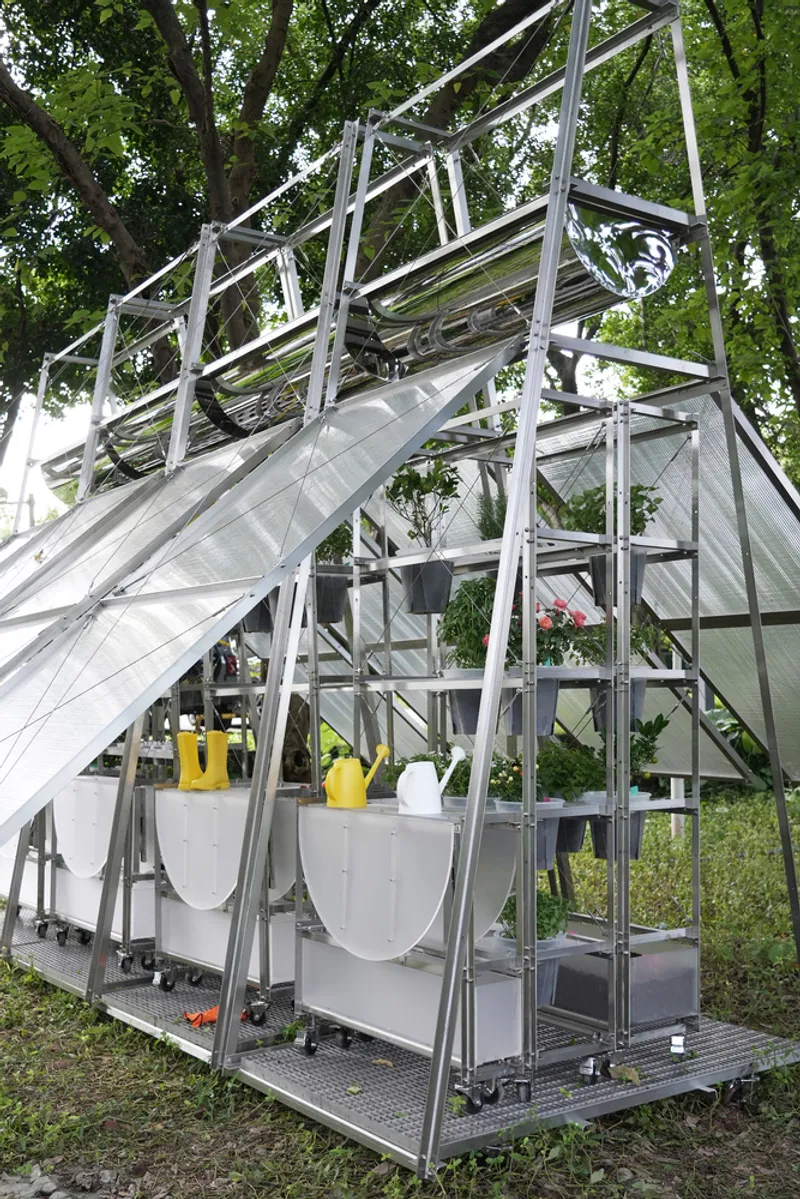 Angled steel frame greenhouse with translucent polycarbonate panels and hanging planters beneath a leafy canopy