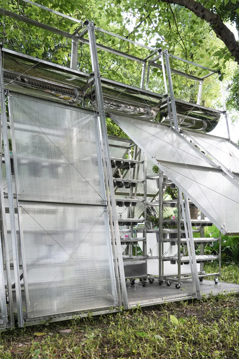 Detail of the angled translucent wall panels meeting the tubular steel structure with foliage beyond