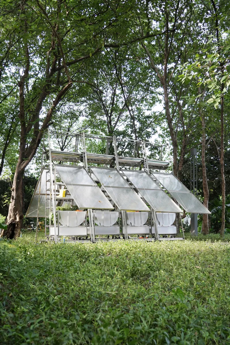Long view of the portable greenhouse structure with tilted roof panels in a clearing among trees