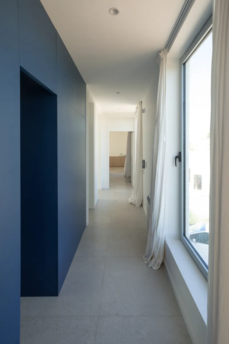 Interior corridor with dark blue painted wall and full-height windows with white curtains