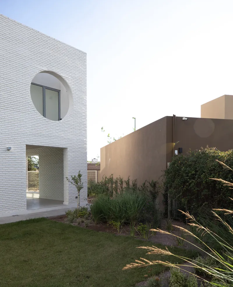 White brick facade with circular window and arched passageway opening to planted garden