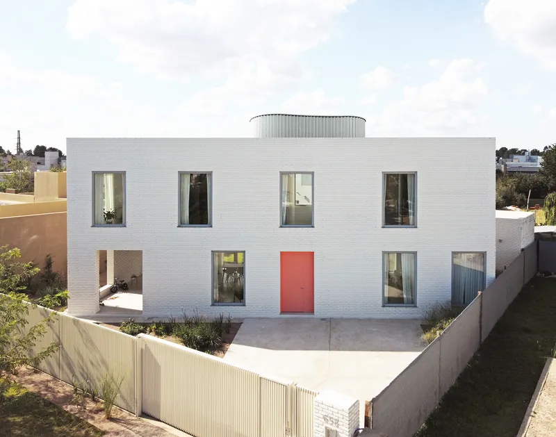 Street view of the white brick facade with red entrance door and cylindrical rooftop element