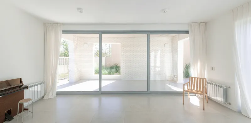 Interior room with full-height glazing overlooking the white brick courtyard and garden