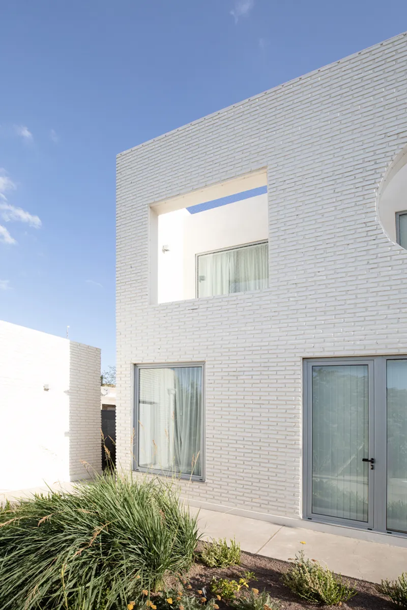 White brick facade with recessed balcony and planted beds along concrete terrace under blue sky