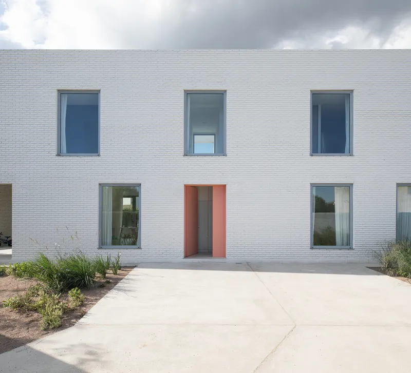 White brick facade with recessed coral entry door and concrete approach under partly cloudy skies