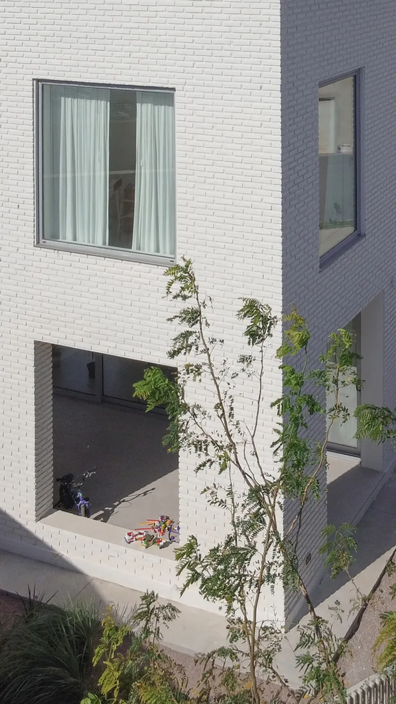 Overhead view of courtyard with young tree and figure on concrete paving between white brick volumes