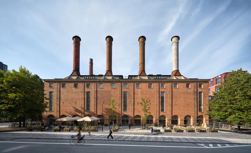 Street view of the red brick facade with five tall chimneys and arched openings at ground level