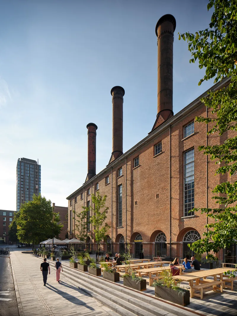 Outdoor seating area with timber benches and planters facing the brick facade with three chimneys