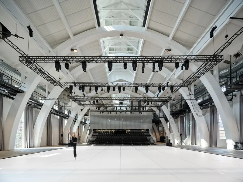 Event hall with steel truss lighting grid, white structural ribs, and pitched roof with skylights