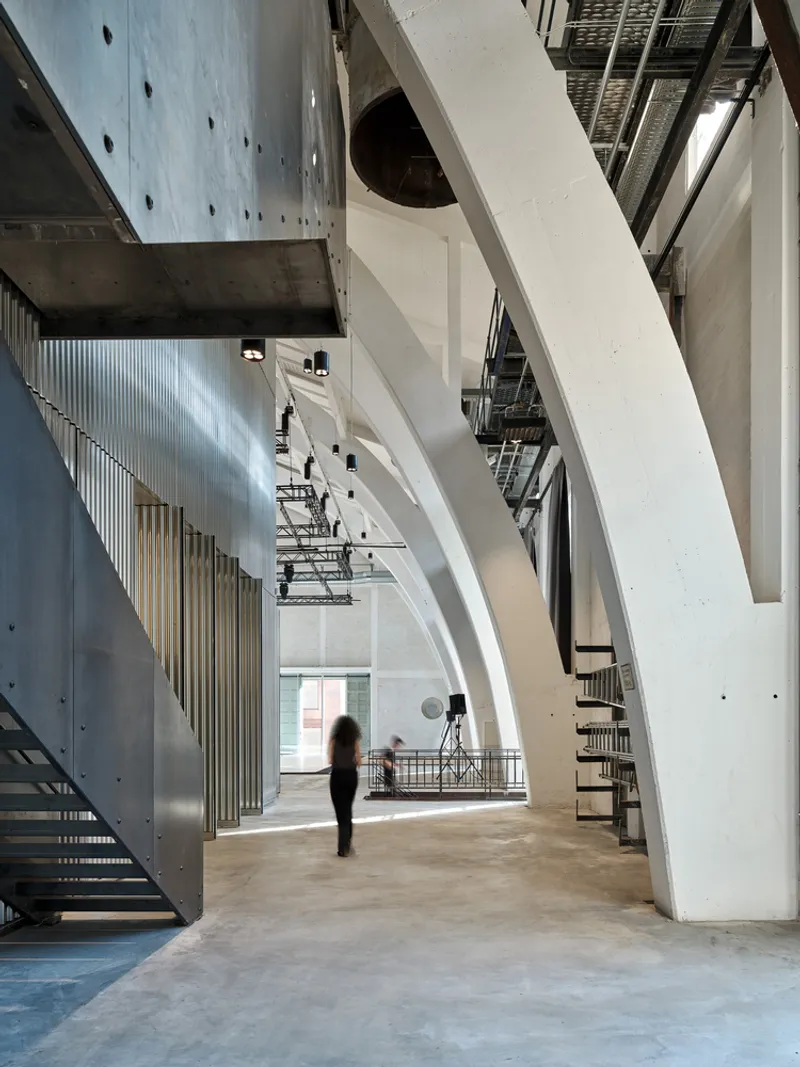 Interior hall with angled white beams, exposed concrete ceiling, and a figure in motion beneath