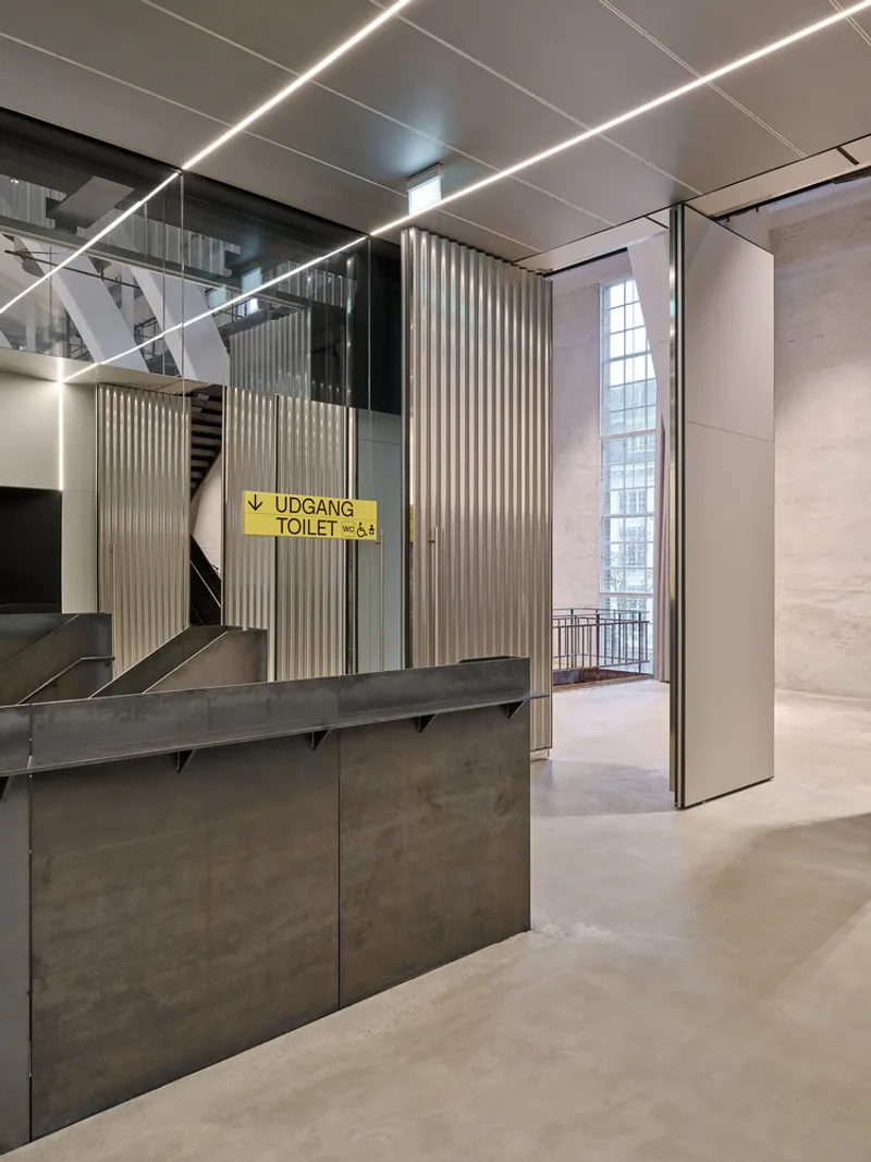 Foyer with stone-clad reception desk below linear ceiling lights and a yellow wayfinding sign