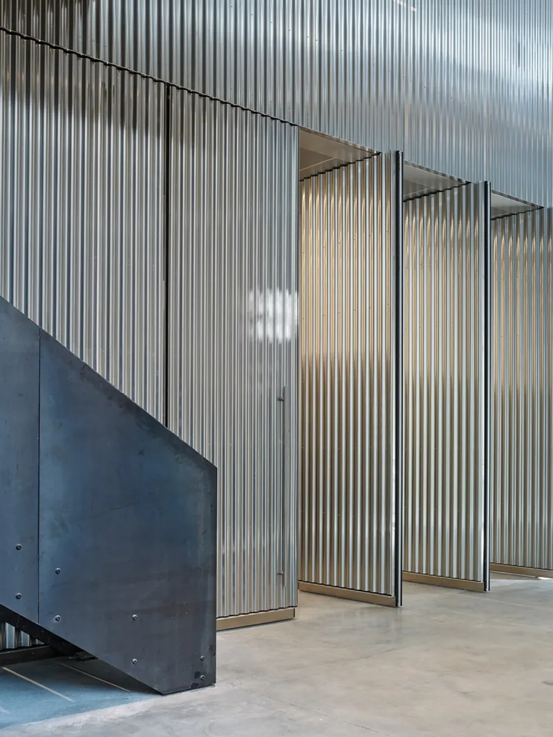 Folding corrugated metal screen panels arranged in series beside a steel staircase volume