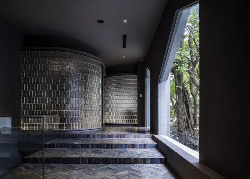 Curved patterned block walls flanking herringbone tile steps beneath a sloped black ceiling