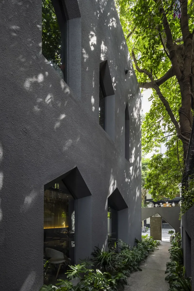 White stucco facade with house-shaped window openings amid dappled tree shadows