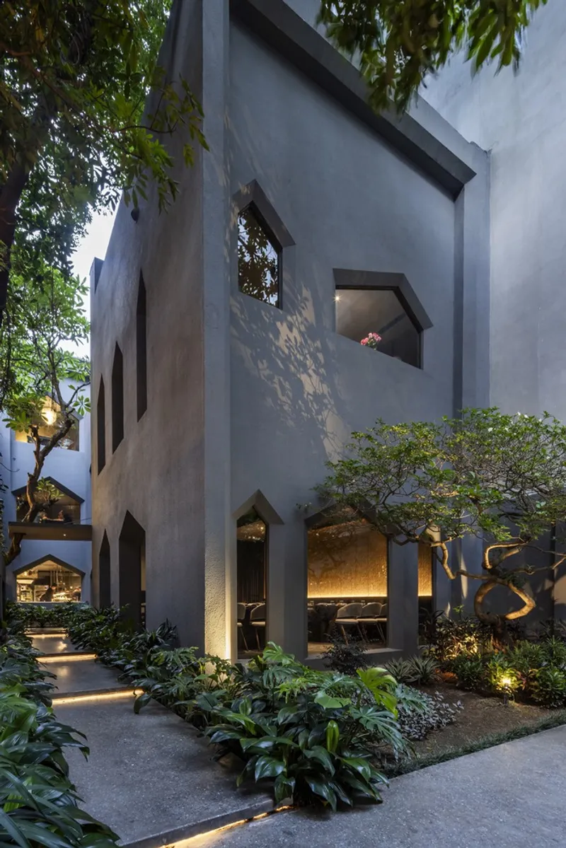 Courtyard view of grey concrete volumes with pointed openings glowing at dusk