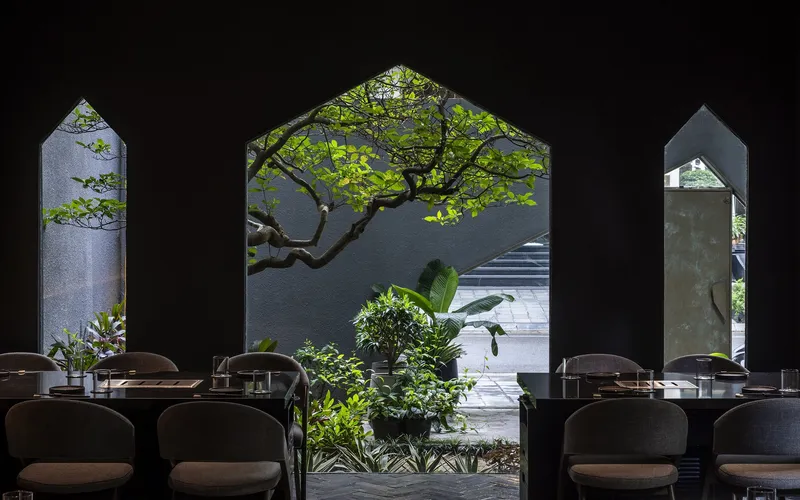 Interior view through pointed archways framing courtyard tree and stone staircase beyond