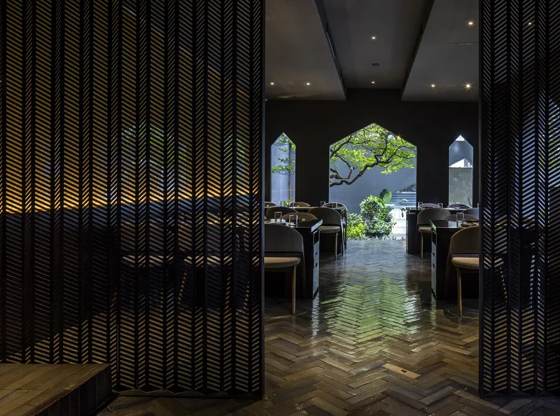 Herringbone timber floor between chevron-patterned screens framing house-shaped openings to garden