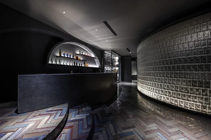 Bar area with curved glass block wall, herringbone wood flooring, and arched bottle display alcove