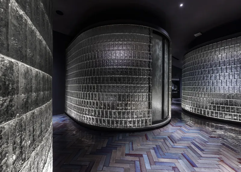 Corridor showing cylindrical glass block volume, textured concrete wall, and chevron pattern wood floor