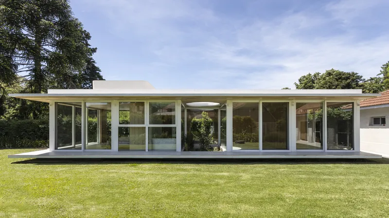 Garden facade with continuous glass walls and flat roof overhangs surrounded by lawn and mature trees