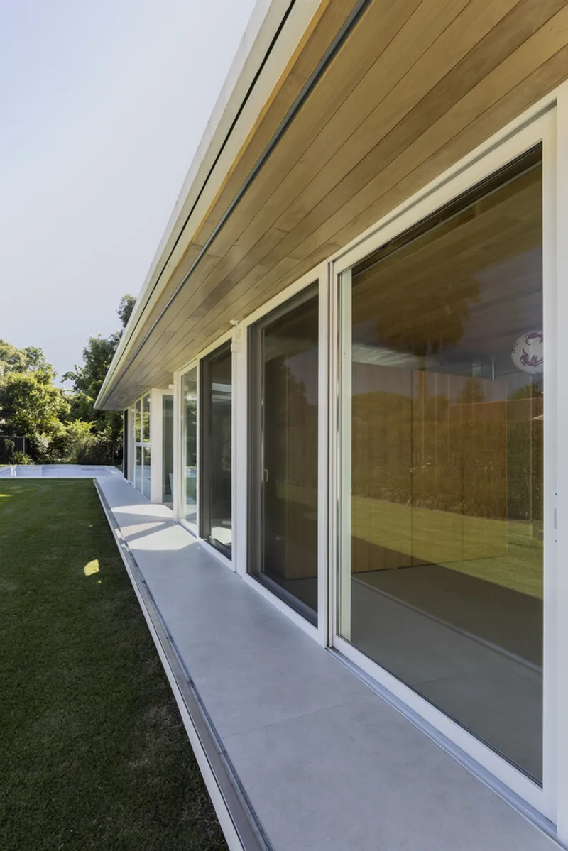 View along the concrete terrace showing the rhythm of sliding glass panels beneath the timber ceiling