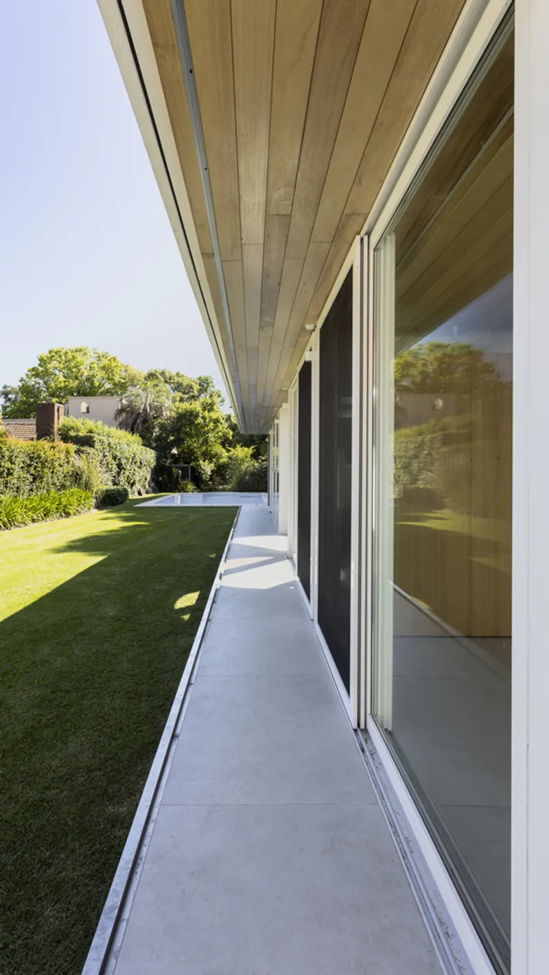 Covered walkway with timber plank soffit and sliding glass doors opening to the lawn in afternoon light
