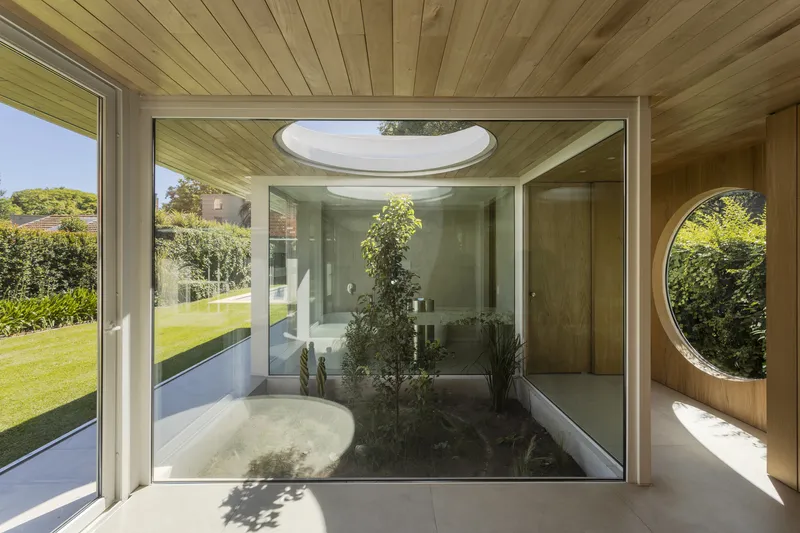 Interior view of the glazed courtyard with planted bed beneath an oval skylight and timber-lined walls