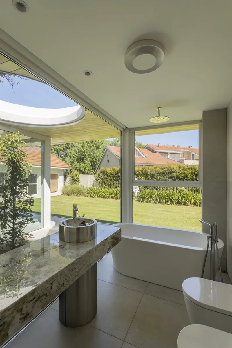 Bathroom with freestanding tub and circular skylight overlooking a lawn and neighboring houses