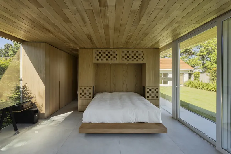 Bedroom with timber-clad ceiling and integrated headboard wall opening to a garden terrace