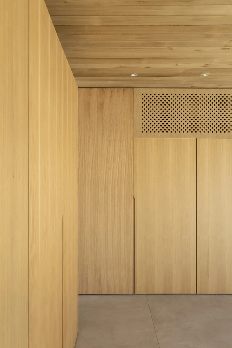 Detail of timber wall panels with perforated ventilation grille above built-in storage