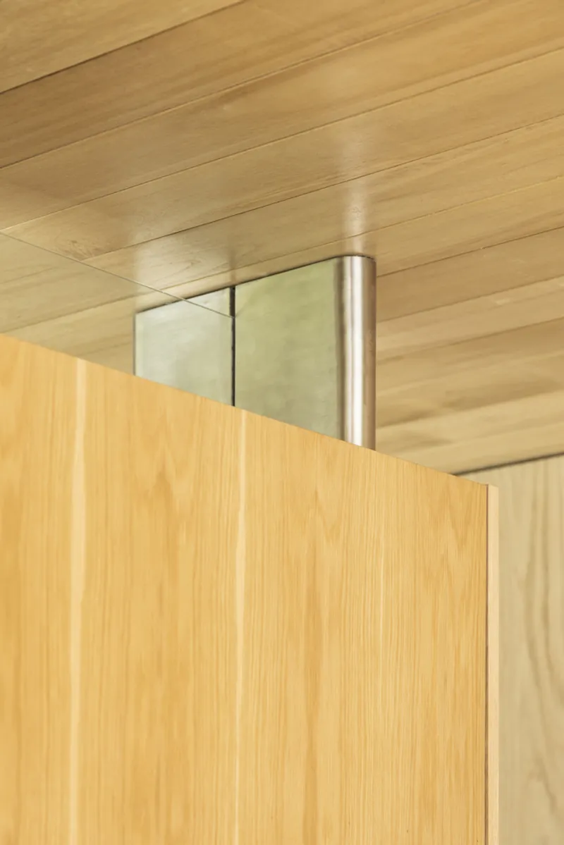 Detail of a cylindrical steel hinge connecting wood panels beneath a timber ceiling