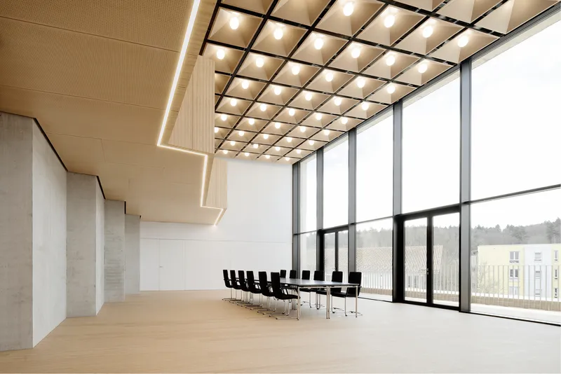 Double-height meeting room with gridded luminous ceiling panels and floor-to-ceiling glazing overlooking distant fields