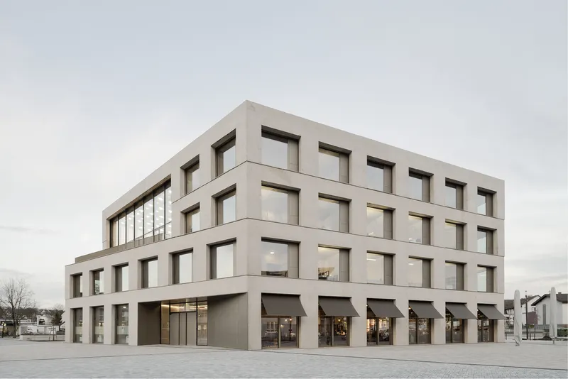 Four-story facade with deep-set square windows and ground-level retail openings under an overcast sky