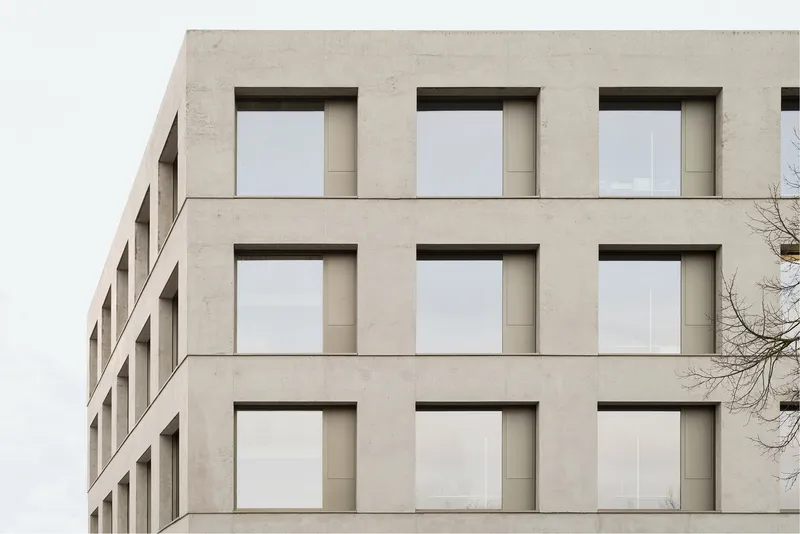 Close-up of the precast concrete facade with recessed window frames and bare tree branches