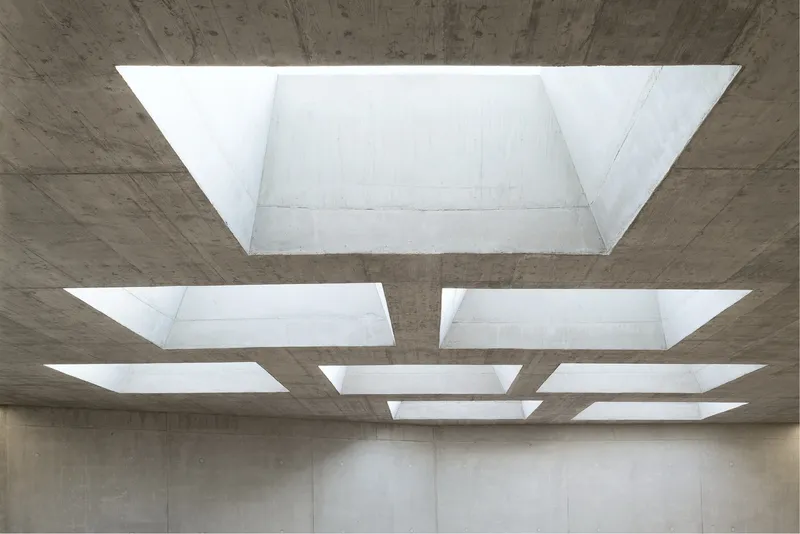 Grid of rectangular skylights set into a board-formed concrete ceiling illuminating the interior below