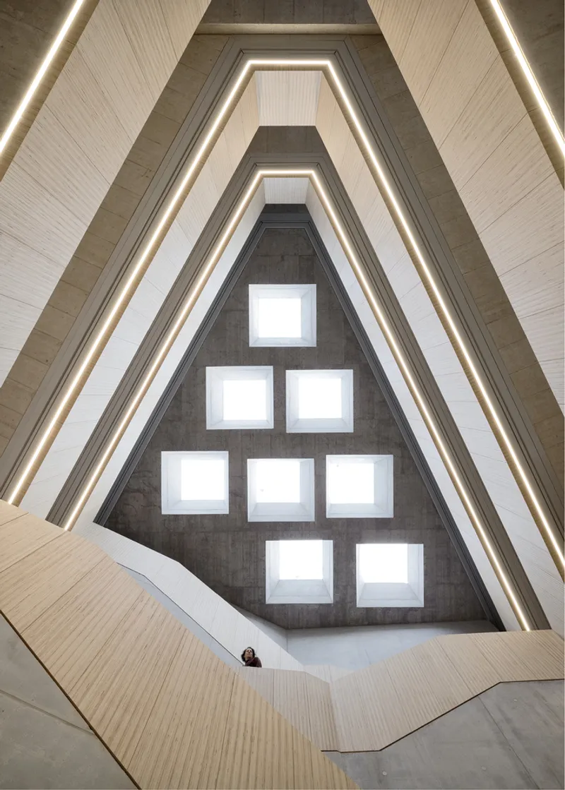View up through a triangular atrium with integrated linear lighting and square skylights puncturing the concrete end wall