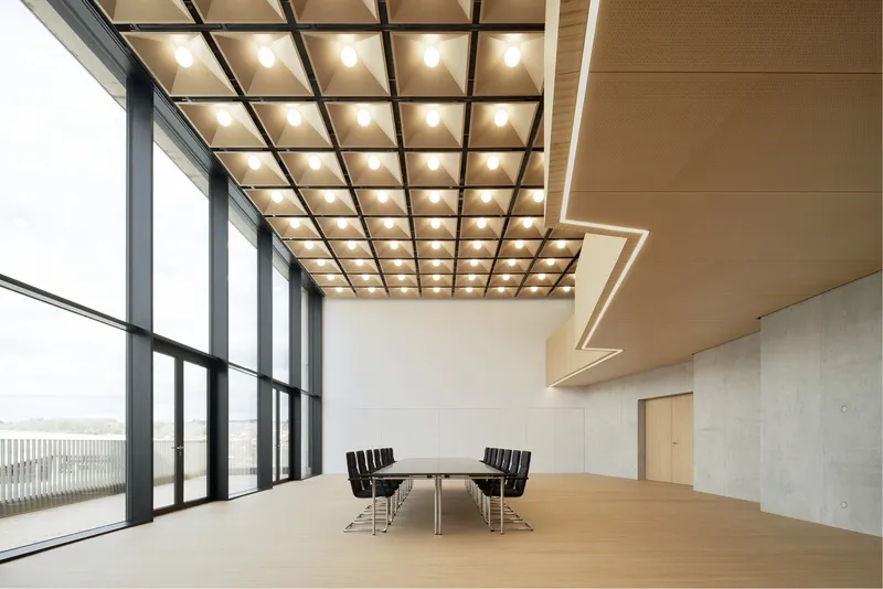 Open meeting space with black-framed glazing, gridded luminous ceiling, and timber-clad soffit