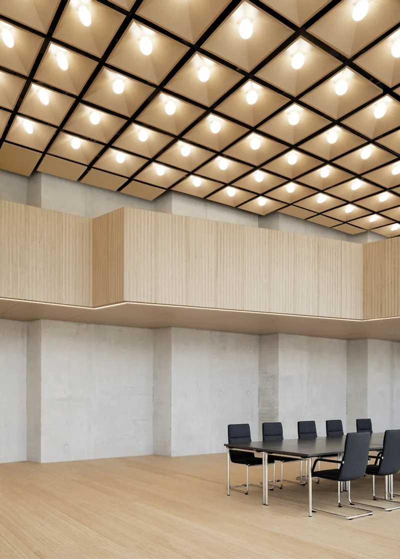 Conference room with black gridded ceiling panels, integrated lighting, and board-formed concrete walls