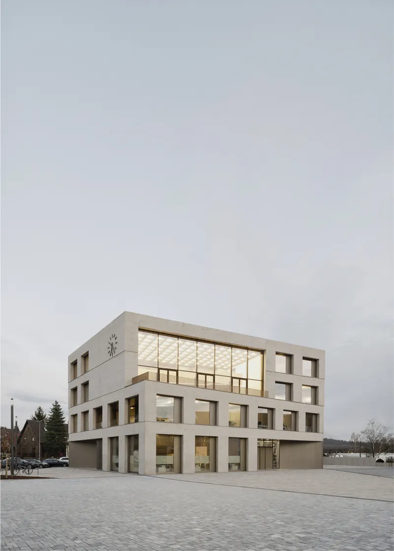 Concrete facade with rhythmic window openings and illuminated upper level at dusk